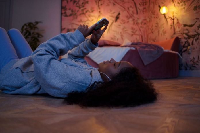 Adolescente usando un teléfono móvil en la oscuridad de un dormitorio por la noche